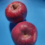 Two red Jumla apples on a blue surface.