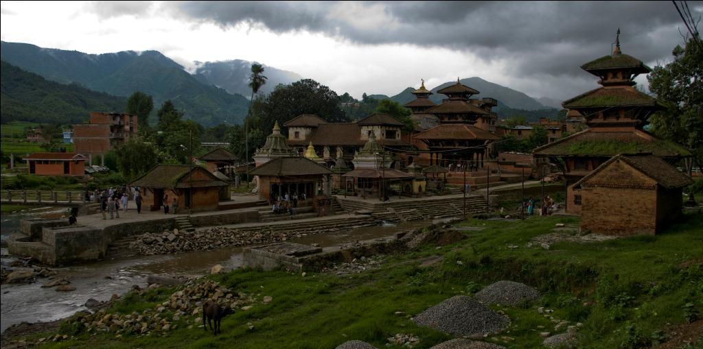 Panauti’s temple quarter beside the river, with pagoda roofs and green hills under cloudy skies.